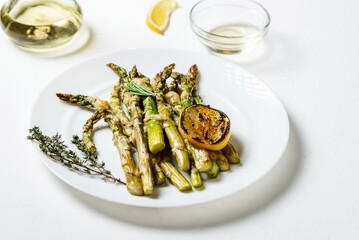 Asparagus baked with cheese, herbs and spices with lemon on a white plate. White background. Vegetarian food. Healthy food.