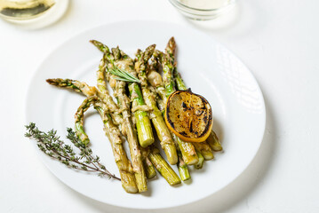 Asparagus baked with cheese, herbs and spices with lemon on a white plate. White background. Vegetarian food. Healthy food.