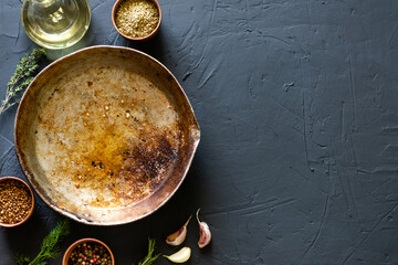 Empty old frying pan surrounded by spices on a dark background. Place for text. Cooking concept.