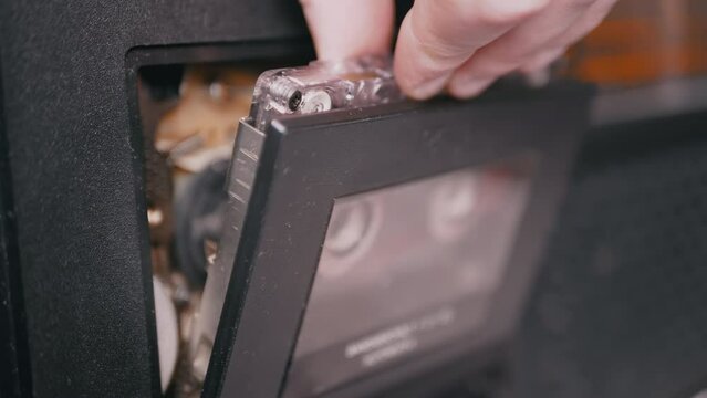 Female Hands Take Out an Old Audio Cassette from a Vintage Tape Recorder. Classic black retro 90s magnetic tape cassette for listening to music. Disco 80s, 90s disco style. Portable stereo player.