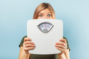 Beautiful blonde woman satisfied with her diet results holding white scales on blue background