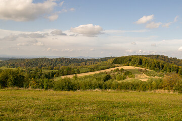 Landscape overlooking high mountains and glades. In the distance a strip of trees and buildings.