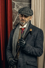 Mysterious retro 1920s english gangster with flat cap, grey coat and a fighting cane