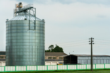 A large modern plant for the storage and processing of grain crops. view of the granary on a sunny day. Large iron barrels of grain. silver silos on agro manufacturing plant for processing and drying