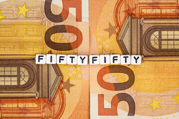 Two 50 eur banknotes and small cube beads with text FIFTYFIFTY, closeup detail from above