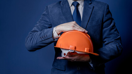 Close-up of a businessman or engineer holding a helmet in his hands on a blue background