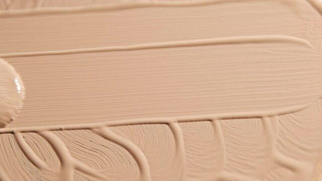 Smear foundation face cream or beige concealer smudge with cosmetic brush. Make-up textured background.