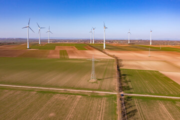 Ein Strommast und viele riesige Windräder auf einem ländlichen Acker von oben als Drohnenaufnahme...