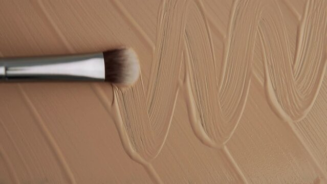 Foundation close-up, sliding cosmetic brush. Texture of foundation close-up. Advertising of decorative cosmetics. Beige paint.