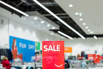 A sign with the inscription SALE in white on a red background in the trading floor of casual clothing store. Fashion concept, discount season, black friday, offline shopping, gimmicks, holiday sales.