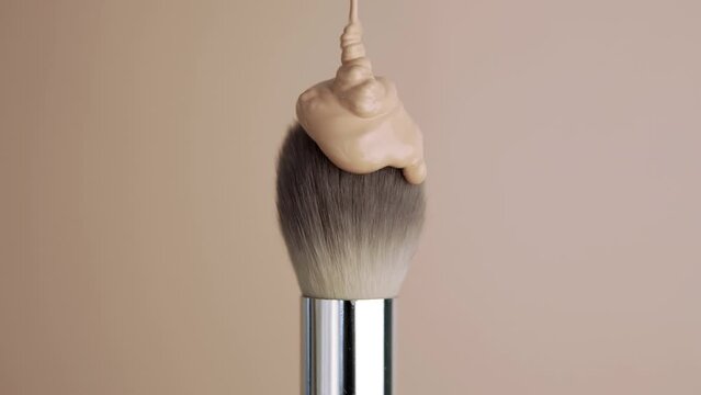 The foundation is poured onto the makeup brush. Decorative cosmetics advertising concept. Brush on a beige background.