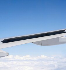 View of above clouds and wing of airplane with open flaps from window with blue sky background. Use for wallpaper or backdrop.