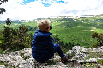 Naklejka na ściany i meble A little boy on the background of the alpine meadows of the Lago-Naki plateau in Adygea. Russia. 2021.