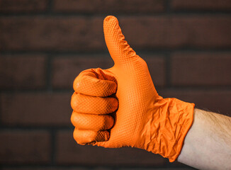 The hand of a young man in a rubber glove on an isolated background of a brick wall in close-up,...