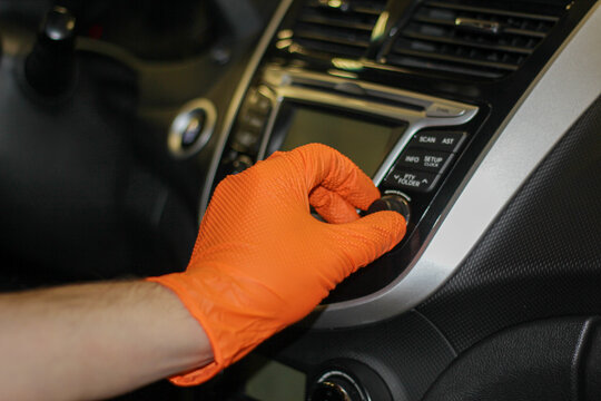 The concept of transport and vehicle is a person using a car audio system. A close-up photo of a man's hand in rubber gloves controlling the multimedia of a car.