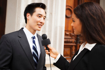 A woman with a microphone interviews a well dressed man. Could be politician, business or other professional.
