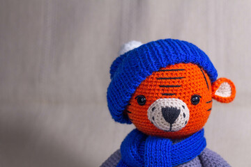 Soft knitted toy tiger portrait in a blue hat on a gray background