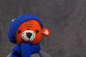 Soft knitted toy tiger portrait in a blue hat on a gray background
