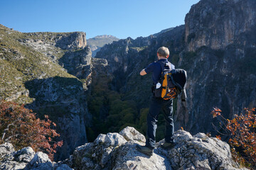 Obraz premium A rear view of a Caucasian male traveler standing on rocks taking picture of the rocky cliffs