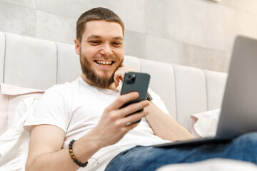 young man at home on the couch with a laptop looking at the phone