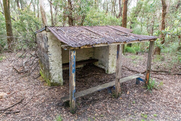 Photograph of an old and damaged white stone shelter in a forest