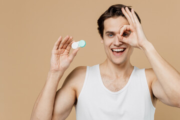 Attractive young man 20s perfect skin wear undershirt hold contact lenses case container cover eye...