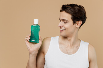 Attractive satisfied young man 20s perfect skin in undershirt hold tooth mouth rinse bottle isolated on pastel pastel beige background studio portrait Toothcare healthcare cosmetic procedures concept
