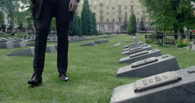 Sad young man in suit stands on the grave of the city cemetery. Funeral and farewell, honoring the passed relatives, 4k 60p Prores