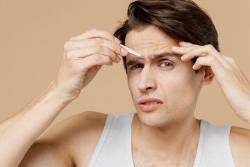 Attractive european young man 20s perfect skin in undershirt pluck out hair with tweezers isolated...