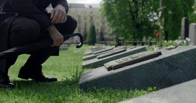 Sad young man in suit stands on the grave of the city cemetery. Funeral and farewell, honoring the passed relatives, 4k 60p Prores