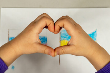 A child makes a heart sign with his hands over a drawing of two flags of Ukraine and Russia close-up. View from above. Children against war.