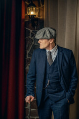 An elderly man in a stylish tweed suit, a flat cap and a cane. Peaky blinders style.