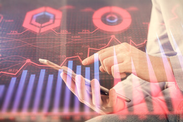 Double exposure of man's hands holding and using a digital device and forex graph drawing. Financial market concept.