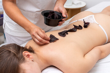 Massage session for a young woman, relaxing and harmonics in a beauty center with balls, algae, aromatic oils and reiki stones, performed by a beautician.