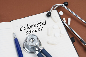 On a brown surface lie pills, a pen, a stethoscope and a notebook with the inscription - Colorectal...