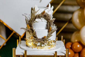 Sweet gold coloured christening cake with angel wings and natural ornaments in restaurant after baptism ritual