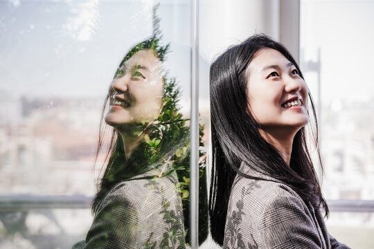 Portrait Of Successful Chinese Business Woman Smiling In Office. Reflection On Glass