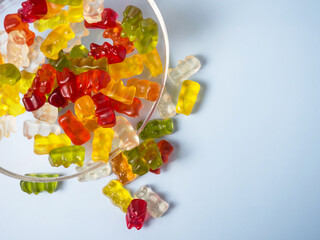 Bowl with tasty bright gummy bears on blue table