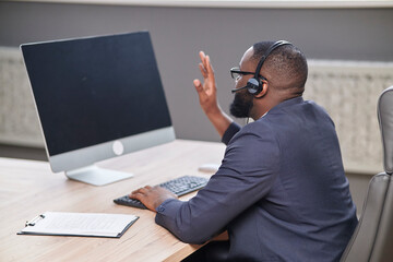 African american man working on computer blank monitor , with headphones. Video conferencing coaching