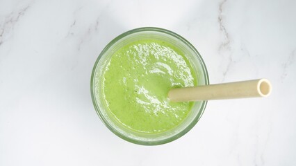 Green tasty smoothie with bamboo straw photographed from above