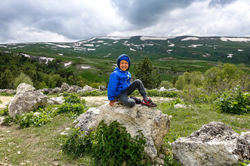 Fototapeta premium A little boy on the background of the alpine meadows of the Lago-Naki plateau in Adygea. Russia. 2021.
