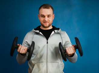 Young active strong man training biceps muscles with heavy dumbbell weight in the gym