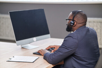 African american man working on computer blank monitor , with headphones. Video conferencing coaching