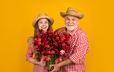 happy old grandfather with granddaughter hold tulip flowers on yellow background. grandparents day