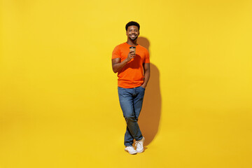 Fototapeta na wymiar Full body young man of African American ethnicity 20s wear orange t-shirt hold takeaway delivery craft paper brown cup coffee to go isolated on plain yellow background studio People lifestyle concept.
