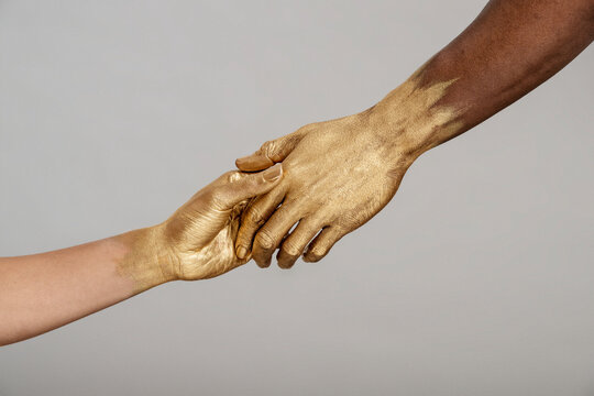 Detail shot of mixed-race woman and Black man with gold painted hands holding hands.