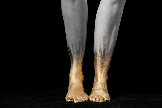 Desaturated/Close-up shot of mixed race and Caucasian women's legs and gold painted feet on black background.