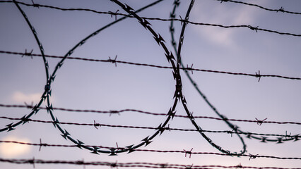 Barbed wire against cloudy blue sky.