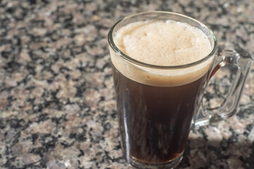 tonic coffee in a transparent cup that is on a marmore table, urban climate in the background