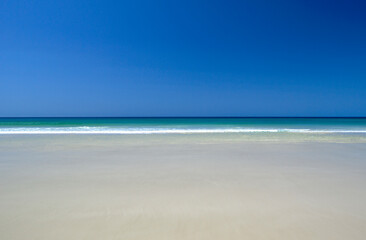 Calm tropical water meets blues sky and pristine sandy beach